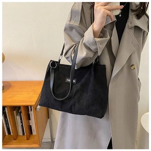 Close-up of black corduroy tote bag showing the fashion label and leather strap