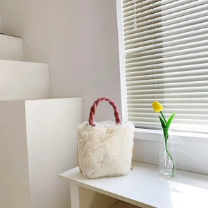 Détail du sac seau en fausse fourrure blanche avec anse tressée rose et chaîne dorée