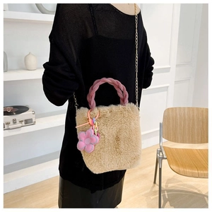 Gros plan d'un sac seau en peluche kaki avec poignée rose et breloque fleurie porté