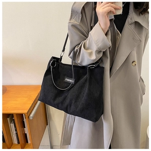 Detail of black corduroy tote bag with vertical stripes and fashion label on shoulder