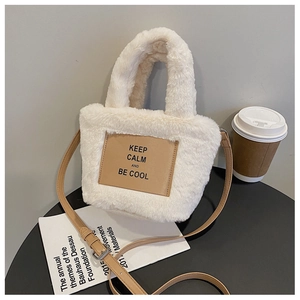 Detail of white plush bucket bag with brown leather strap and Keep Calm label on table