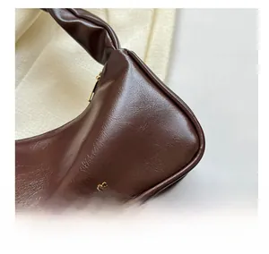 Close-up of pleated dark brown baguette bag with knotted handle and gold zipper detail