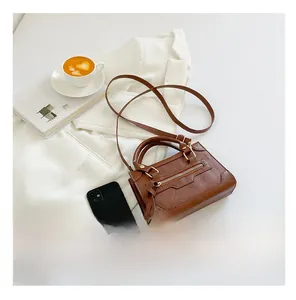 Confronto dimensioni borsa retrò marrone con uno smartphone su blazer bianco