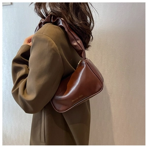 Detail of the brown ruched shoulder strap and fashion gold logo on the chic baguette bag