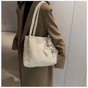 Detail of beige quilted tote bag with woven shoulder strap and silk scarf accessory
