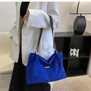 Detailed texture of blue corduroy tote bag with black strap and fashion patch on model