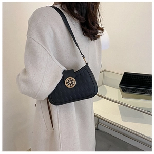 Close-up of black quilted shoulder bag with gold wheel lock worn with a beige wool coat