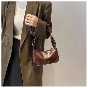 Close-up of brown leather baguette bag featuring a scrunchie handle and gold logo