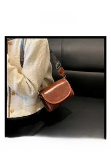 Close-up of vintage brown leather crossbody bag featuring a colorful woven shoulder strap
