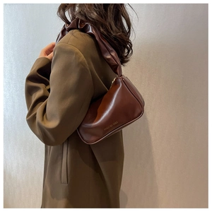 Detail of a dark brown baguette bag with a pleated handle on a model's shoulder