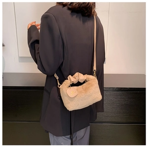 Detail of plush beige handbag with pleated handle and circular leather tag on model