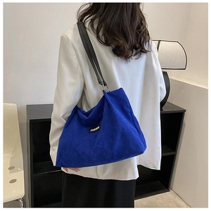 Detail of royal blue corduroy tote bag featuring black leather straps and fashion label