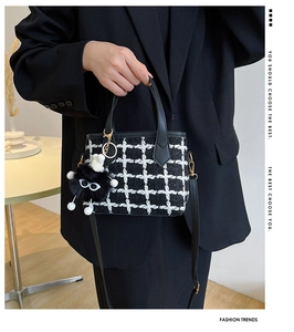Detail of tweed checkered handbag with black leather handle and plush monster charm