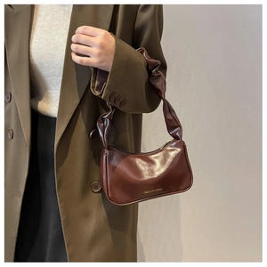 Close-up of brown pleated baguette bag with gold lettering on a stylish green blazer