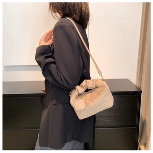 Detail of plush beige shoulder bag featuring a pleated handle and stylish round logo charm