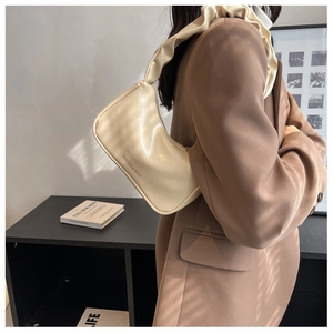 Close-up of beige underarm bag with pleated handle and fashion typography on soft leather