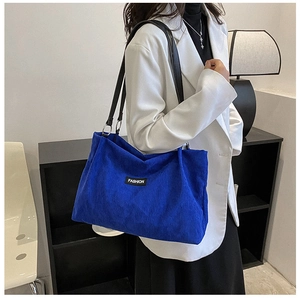 Detail of bright blue corduroy tote bag with black straps and fashion label on a model