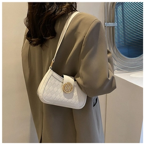 Detail of white quilted leather baguette bag with a gold round lock on model's shoulder