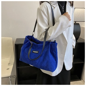Detail view of royal blue corduroy tote bag featuring black leather straps and fashion label