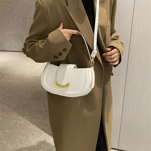 Détail d'un sac bandoulière blanc avec boucle dorée porté sur un blazer sombre
