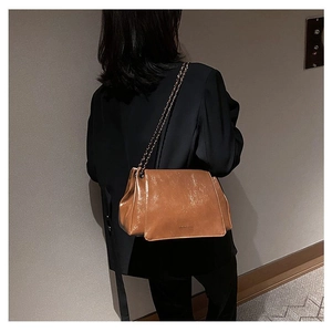Close-up of a brown leather shoulder bag with a glossy pleated texture and metal chain