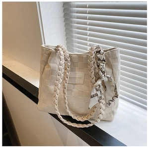 Detail of quilted cream tote bag featuring braided handles and a printed silk scarf