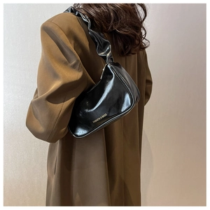 Detail of black patent leather underarm bag with pleated strap and gold fashion logo