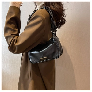Detail of ruffled shoulder strap and gold lettering on a black glossy baguette bag