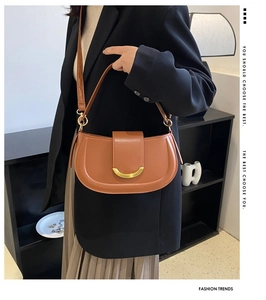 Gros plan du sac besace marron caramel avec boucle dorée porté à l'épaule du mannequin