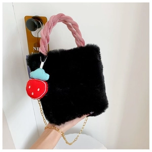 Détail d'un sac seau en fausse fourrure noire avec poignée rose et breloque fraise