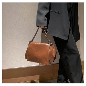 Detail of a brown leather shoulder bag with vintage metal chain and classic flap design