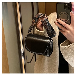 Detail of black saddle bag with white contrast stitching and jacquard strap