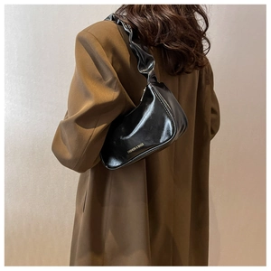 Detail of black glossy baguette bag featuring pleated strap and gold lettering on model