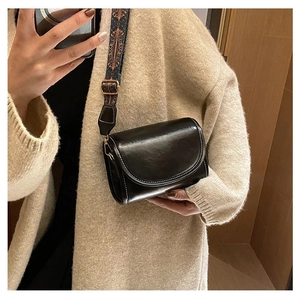 Detail of black crossbody bag with ethnic patterned strap and glossy synthetic leather