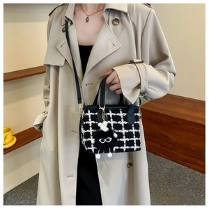 Detail view of a black and white tweed bucket bag with a playful fuzzy eyeball charm
