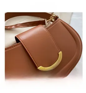 Gros plan sur la boucle métallique dorée semi-circulaire d'un sac besace marron