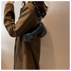 Close-up of black glossy leather underarm bag with unique pleated shoulder strap detail