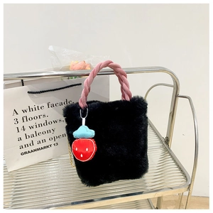 Détail du sac seau en fausse fourrure noire avec anse tissée rose et breloque fraise