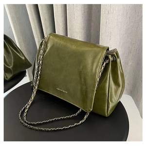 Detail of dark green glossy leather tote with chain strap and metallic logo on table