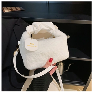 Close-up of white plush handbag featuring gold metal hardware and faux leather handles