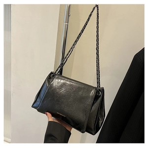 Detail of glossy black leather tote bag with gold logo lettering and metal chain strap