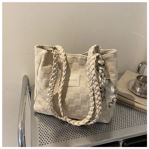 Detail of beige quilted tote bag with woven handles and decorative silk scarf accessory