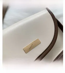 Detailed close-up of cream leather shoulder bag with dark brown edges and gold hardware