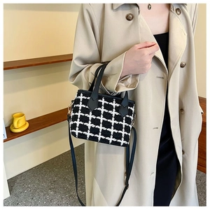 Classic black and white tweed bucket bag with leather strap shown on a beige trench coat