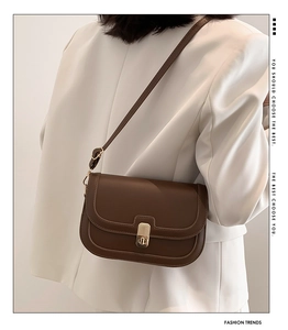Detailed view of brown leather saddle bag with gold buckle on a white blazer