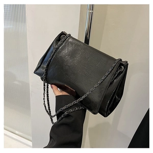 Detail of black glossy wrinkled leather tote with dark grey metal chain and logo