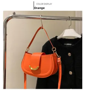 Vue détaillée du sac besace orange avec boucle dorée et bandoulière sur un cintre