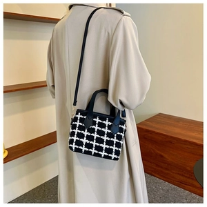 Detailed view of black and white tweed crossbody bucket bag worn with beige coat