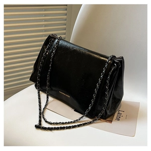 Detail of black glossy PU leather tote with chain strap and gold logo on white chair