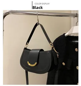 Détail du sac selle en cuir noir avec boucle dorée en croissant sur un support
